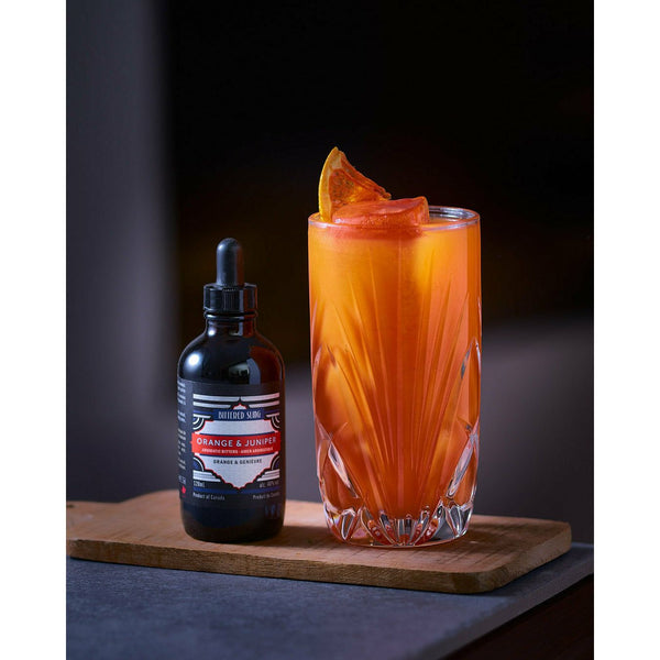 Bittered Sling Orange and Juniper bitters in bottle, next to an orange coloured cocktail.