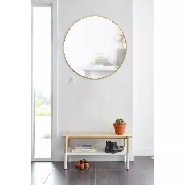 Umbra Hub Wall Mirror in brass, hung on wall above a hall stool.